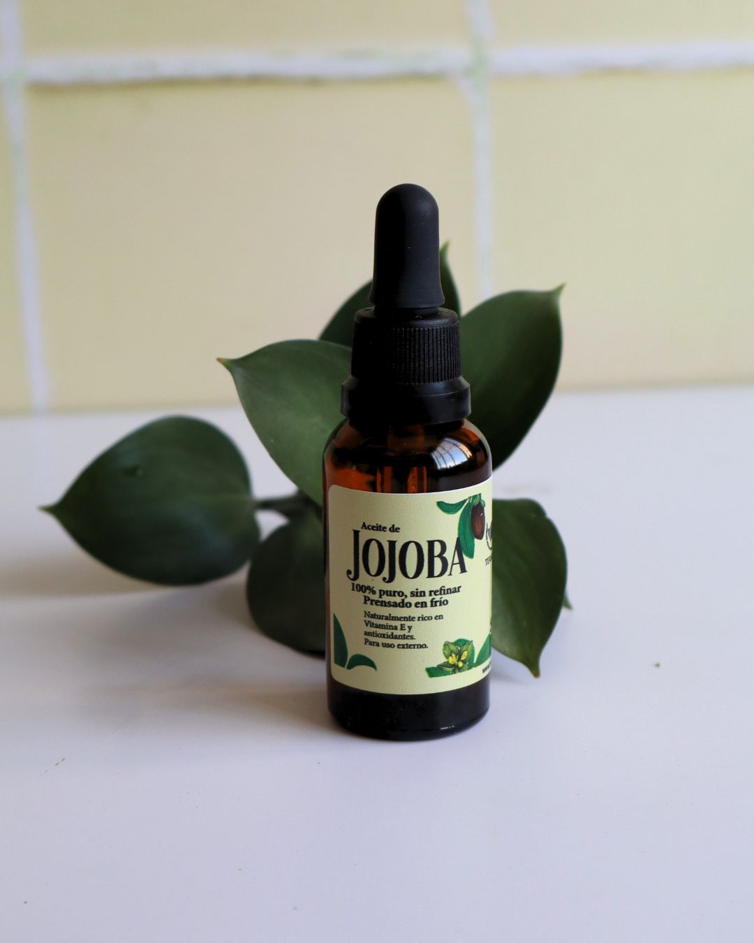 Frasco de aceite de jojoba prensado en frío rodeado de hojas naturales