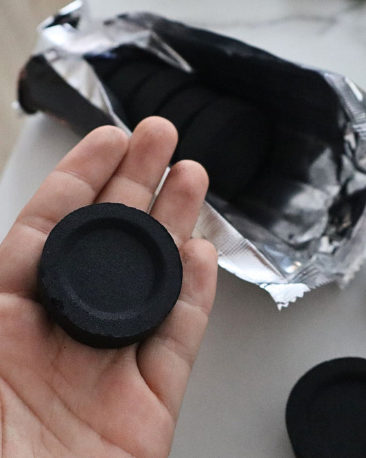 Pastilla de carbón para incienso sostenida en la mano, vista del disco negro